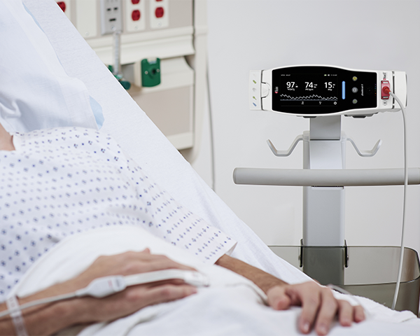 Patient in hospital bed wearing Masimo sensor with Root device in background.