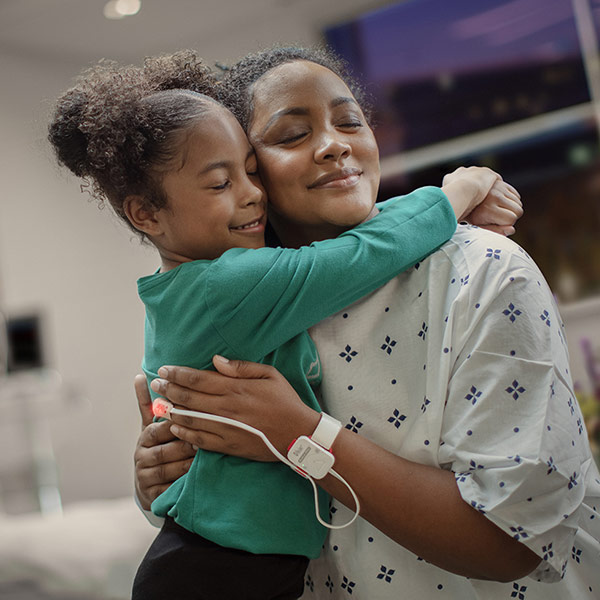 Mère serrant son enfant dans ses bras en milieu hospitalier, tandis qu’un capteur Masimo surveille sa saturation en oxygène.