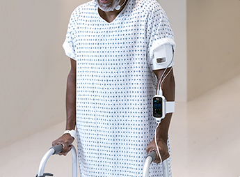 Patient with monitoring devices using walker in a hospital corridor.