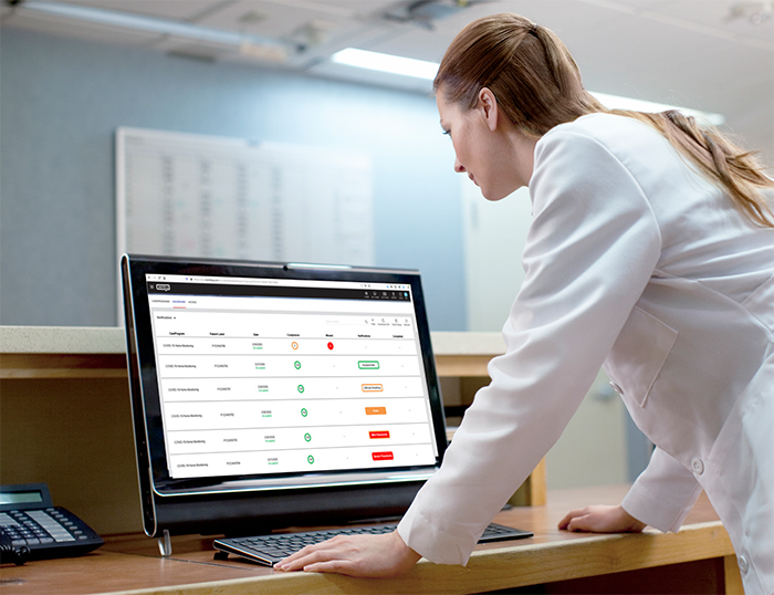 Clinician in white lab coat looking at Masimo SafetyNet Clinician Portal on a computer monitor