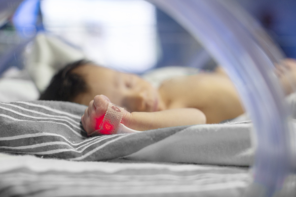 Newborn baby with pulse oximeter sensor on hand glowing red light